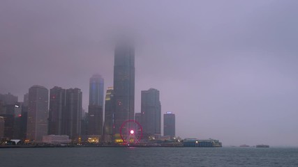 Time lapse day to night of Hong Kong cityscape with hard mist at the harbor in the raining day
