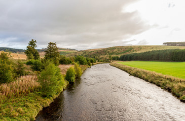 Fototapeta premium A view of the flowing river and low hills in cloudy weather, autumn in Cairngorms National Park
