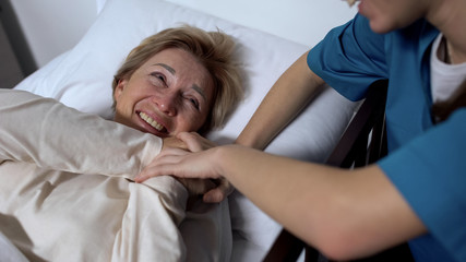 Obraz premium Cheerful patient laughing at jokes of nurse, lying in sickbed, positive mood
