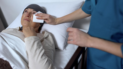 Nurse wiping tears of cancer patient in hospital bed, support and care concept
