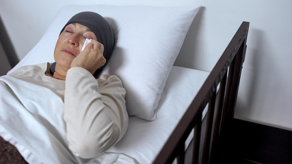 Female patient crying in hospital bed, wiping tears with handkerchief, cancer