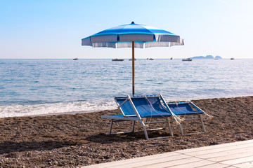 Mediterranean beach. Umbrella with chairs on the stony beach near the sea. Summer holiday and vacation ending