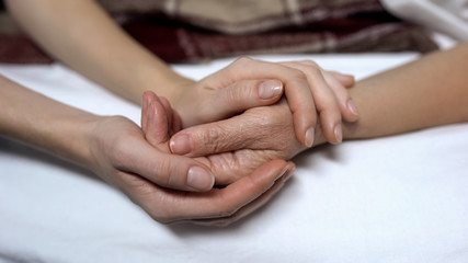 Warm daughters hands holding and calming down sick mother in bed, assistance - obrazy, fototapety, plakaty
