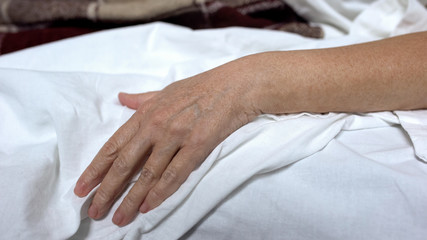 Fototapeta na wymiar Senior woman hand on bed linen, lying in sick bed, suffering illness, death risk