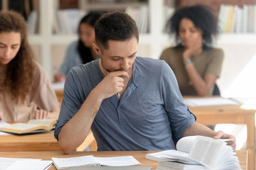 Diverse students absorbed reading textbook studying sitting at desks