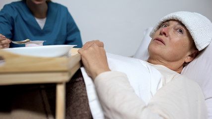 Obraz premium Sick-nurse feeding disabled woman with compress on forehead, hopelessness