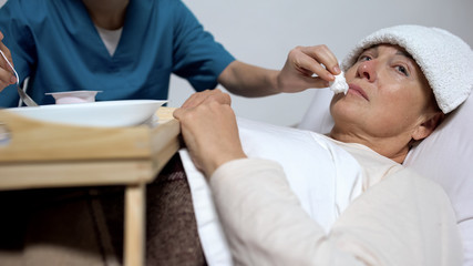 Hospice worker helping to eat mentally disabled elderly woman, healthcare