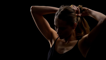 Confident woman taking hair into ponytail against dark background, female power