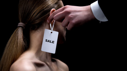 Male hand putting sale tag on female ear, illegal women trafficking, sex slavery