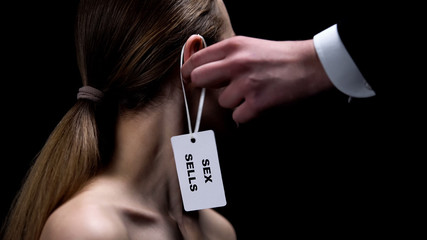 Male hand putting sex sells tag on female ear, sexual slavery, human rights