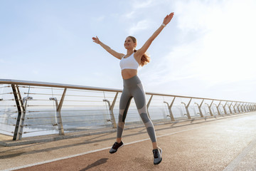 Sportive happy lady jumping up on foot bridge