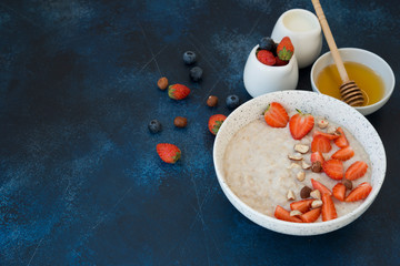 Healthy oatmeal for Breakfast with honey, nuts and summer berries on a blue concrete background.