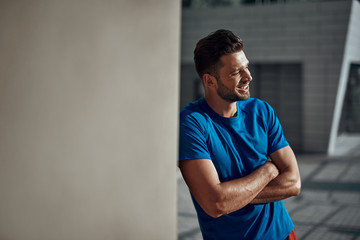 Sportive man standing near wall and smiling wide