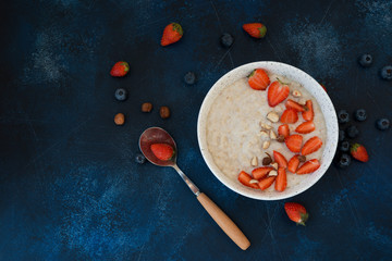 Healthy oatmeal for Breakfast with honey, nuts and summer berries on a blue concrete background.