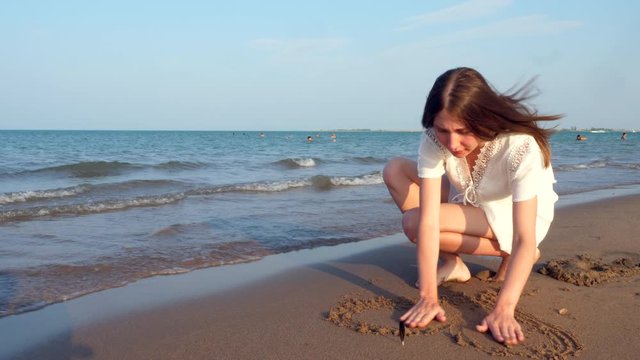 Lonely teen girl draws a heart in the sand