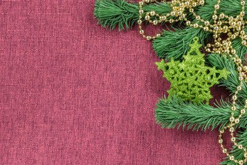 The background is in the form of Christmas tree decorations - a green star, golden-colored beads and artificial fir branches on a burgundy fabric surface, to the left is an empty space