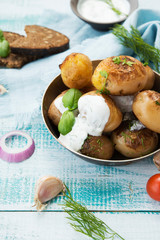 Fried potatoes in a pan with sour cream on rustic background