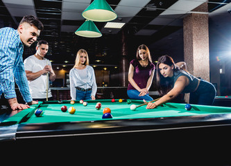 Group of young cheerful friends playing billiards.