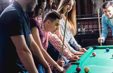 Group of young cheerful friends playing billiards.