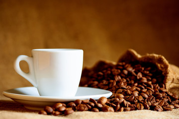White cup and coffee beans on a blurred background.