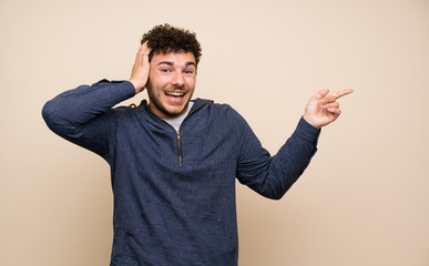 Man with curly hair over isolated wall surprised and pointing finger to the side