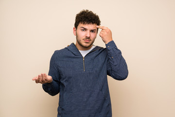 Man with curly hair over isolated wall making the gesture of madness putting finger on the head