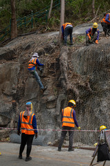 Construction workers are using the mesh to cover the large rocks on the side of the road. In order...