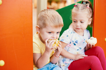 Cute toddler boy and girl is eating donuts outdoor. children is having fun with cakes. Tasty food for kids. Funny time at playground with sweet food. Bright and stylish kids.