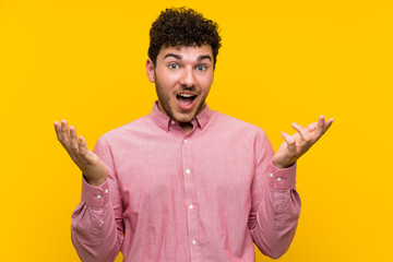 Man with curly hair over isolated yellow wall with surprise facial expression