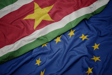 waving colorful flag of european union and flag of suriname.