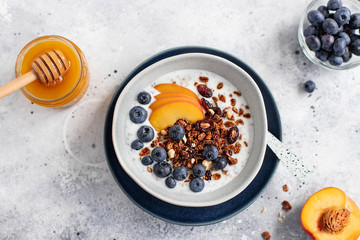 granola with yogurt, blueberries, peach and honey on a light background
