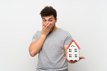 Man with curly hair over isolated wall holding a little house