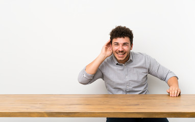 Young man with a table listening to something by putting hand on the ear