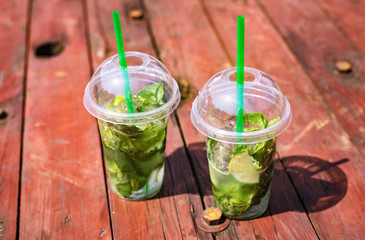 Mojito non-alcoholic, mint lemonade in plastic glasses on a wooden red background