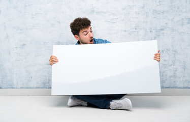 Young man sitting on the floor holding an empty white placard for insert a concept