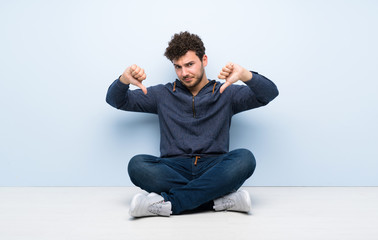 Young man sitting on the floor showing thumb down