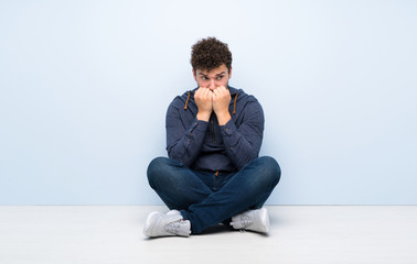 Young man sitting on the floor nervous and scared putting hands to mouth