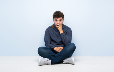 Young man sitting on the floor surprised and shocked while looking right