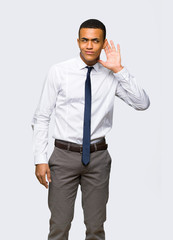 Young afro american businessman listening to something by putting hand on the ear on isolated background