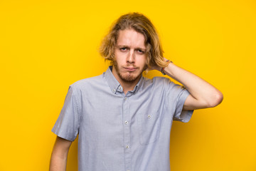 Blonde man over isolated yellow background having doubts