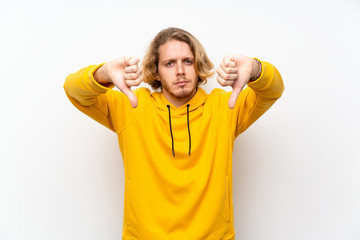 Naklejka premium Blonde man with sweatshirt over white wall showing thumb down