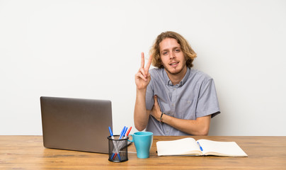 Blonde man with a laptop smiling and showing victory sign