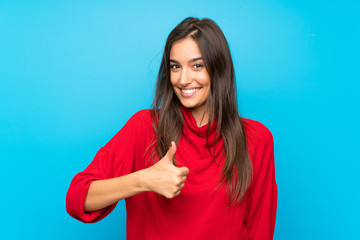 Young woman with red sweater over isolated blue background giving a thumbs up gesture