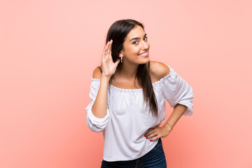 Young woman over isolated pink background listening to something by putting hand on the ear