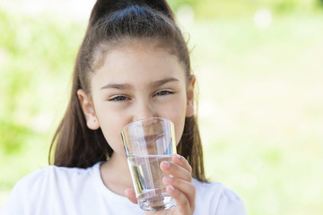 Cute adorable child girl drinking clear water outdoors.