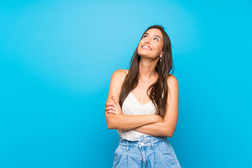 Young woman over isolated blue background looking up while smiling