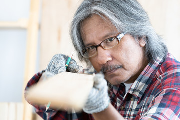 Asian man carpenter working on woodworking table in home carpentry shop, Old asian man works in home carpentry shop.