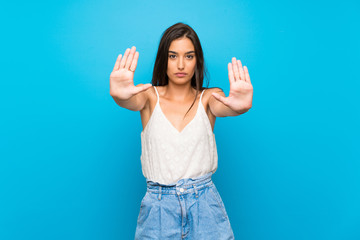 Young woman over isolated blue background making stop gesture and disappointed