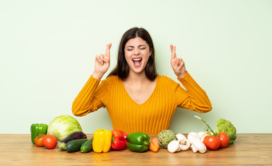 Teenager girl with many vegetables with fingers crossing