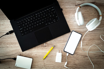 laptop with a portable disk with connected headphones and a smartphone on the desk.  place of relaxation or work.  white phone screen with space for inscription